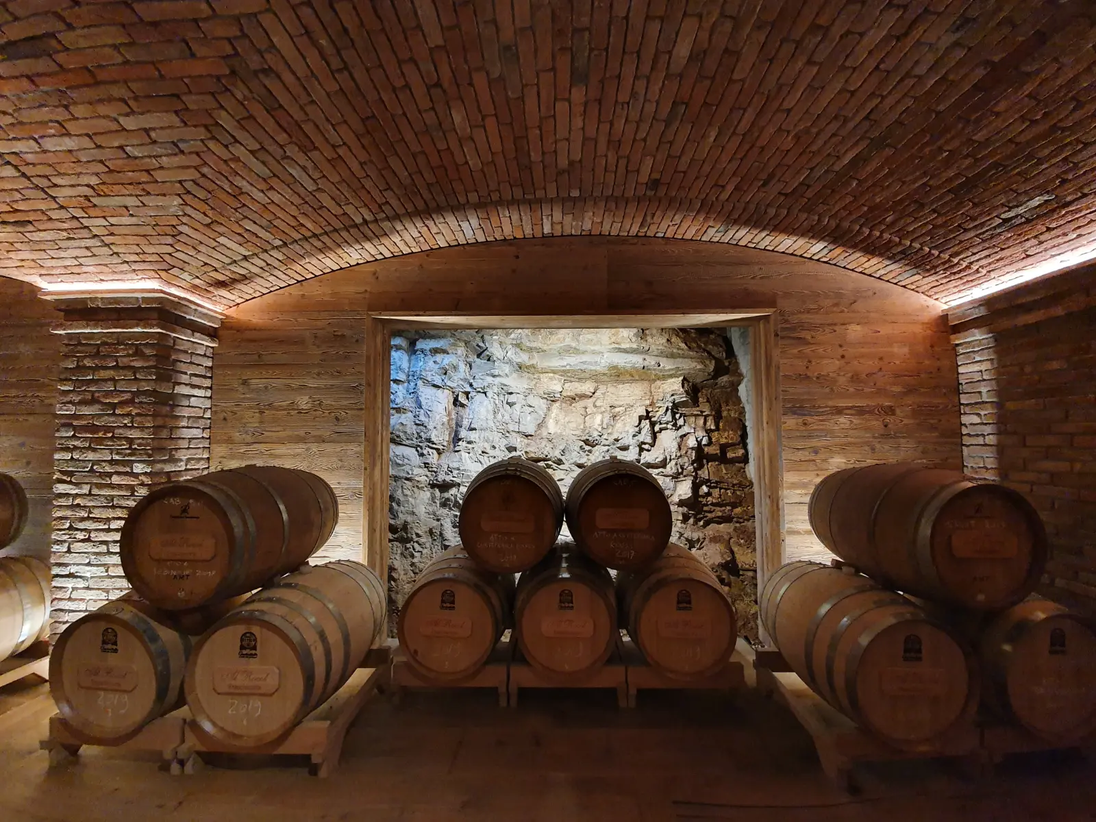 Barrique sotto volte in mattoni davanti alla roccia a vista — cantina Al Rocol, Brescia