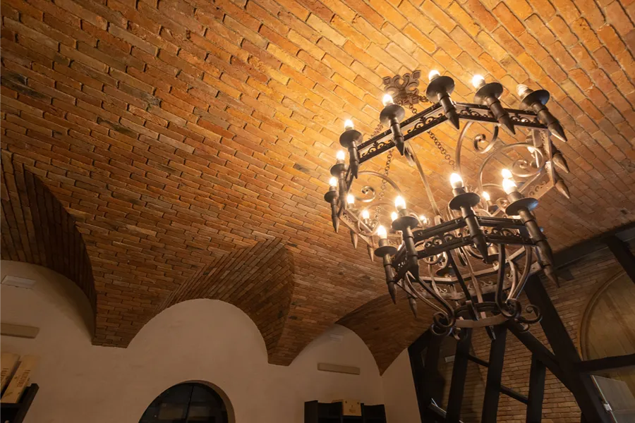 Warm light from a wrought-iron chandelier on the antique bricks of the barrel vault and lunettes — Giusti Wine, Nervesa della Battaglia, Italy