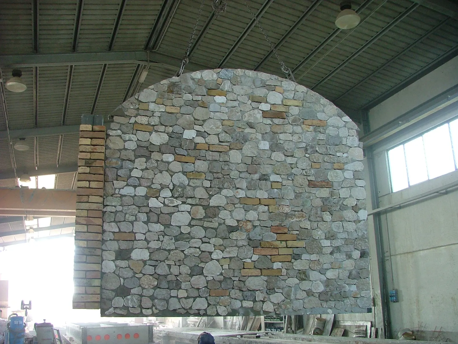 Prefabricated wall panel in split river stone with a curved top edge, lifted in the Pietrantiche workshop