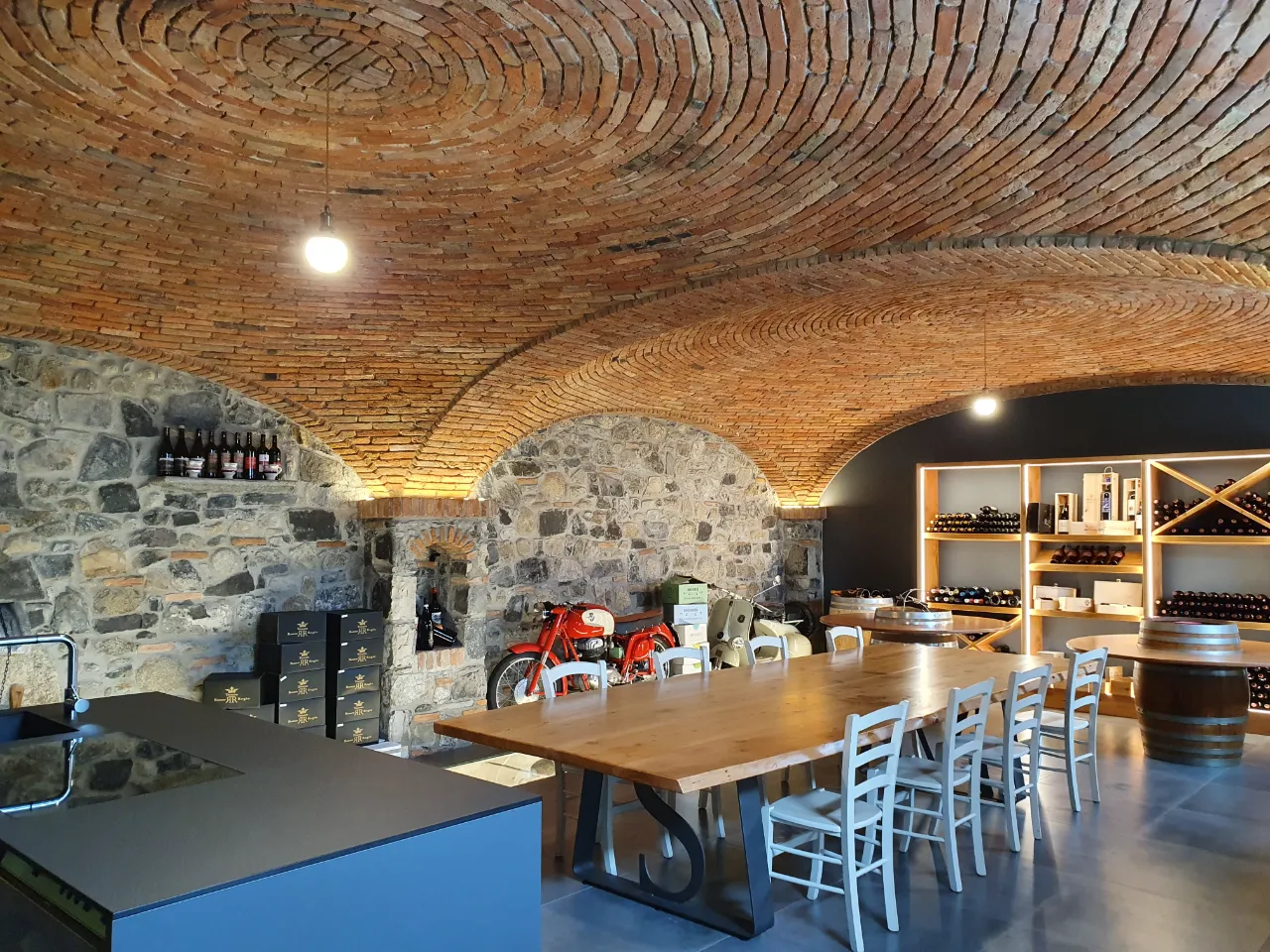 Luxury tasting room featuring two structural masonry sail vaults separated by a central brick arch, combining brick, stone, and wood for an elegant and welcoming atmosphere at Tenuta Ronco Regio.