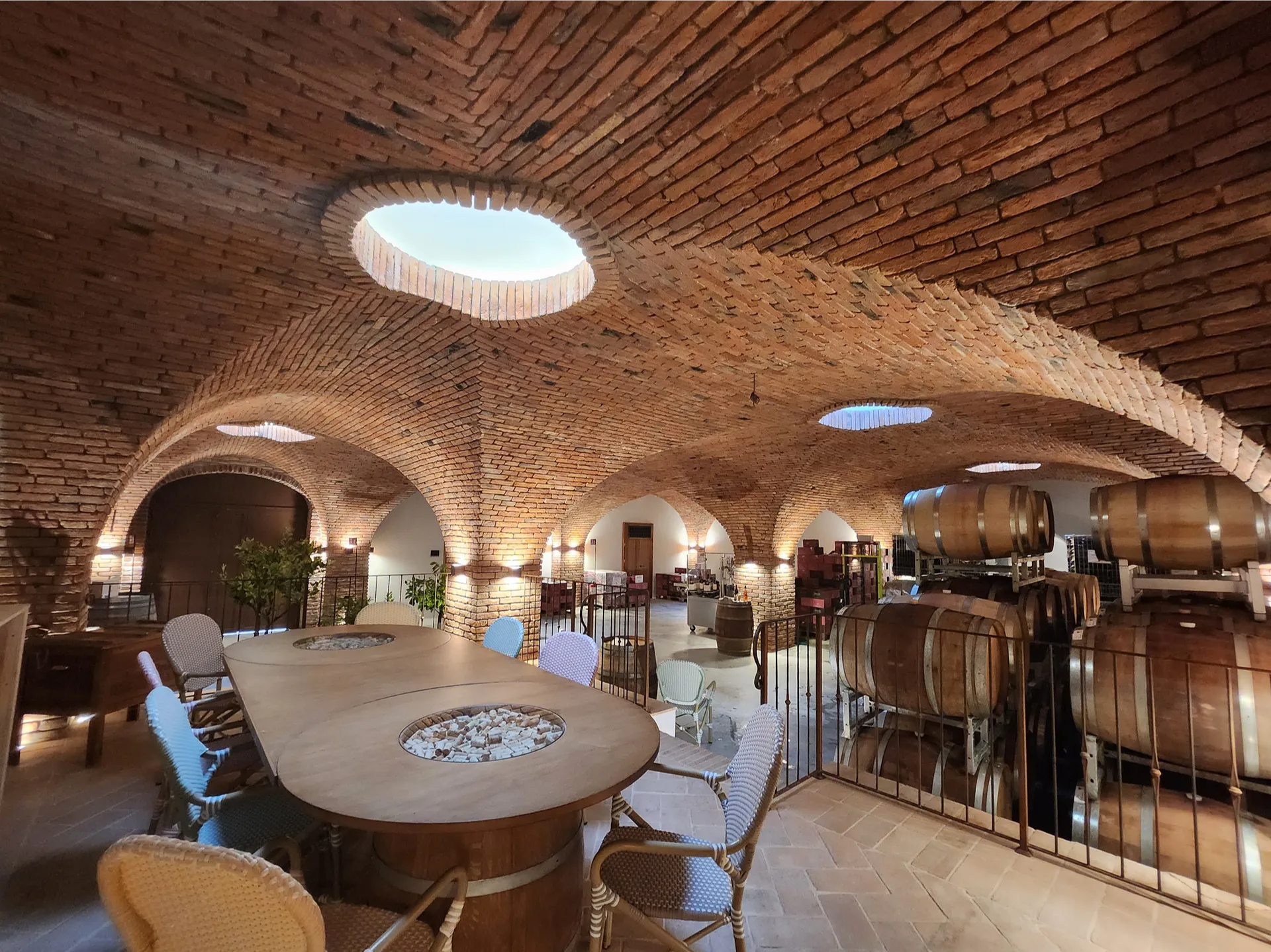 Luxury bespoke wine cellar combining a barrel aging area and an intimate tasting space. The ceiling features intricate brick cross vaults, beautifully illuminated by unique central skylights that create a rhythm of zenithal light and depth, rooted in traditional Italian architecture.