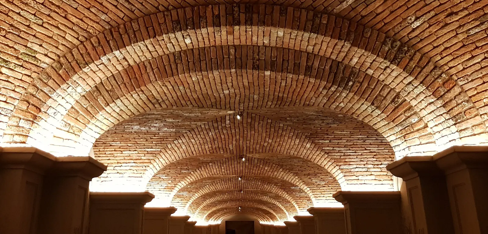 Capitelli con luci a LED nascoste che illuminano dal basso le volte a crociera in mattoni — tunnel Tommasi, Valpolicella